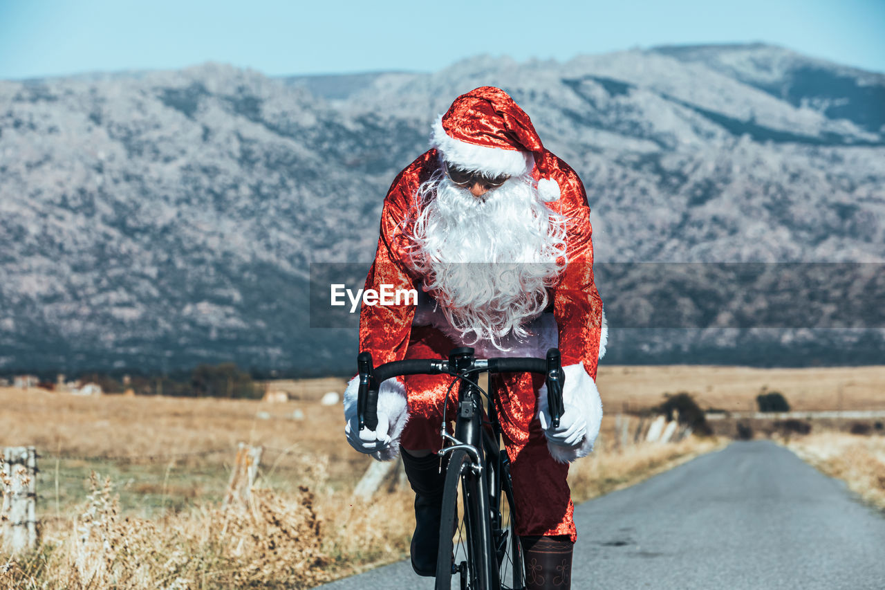 Santa claus in red costume riding modern bike along empty road in highlands on sunny day