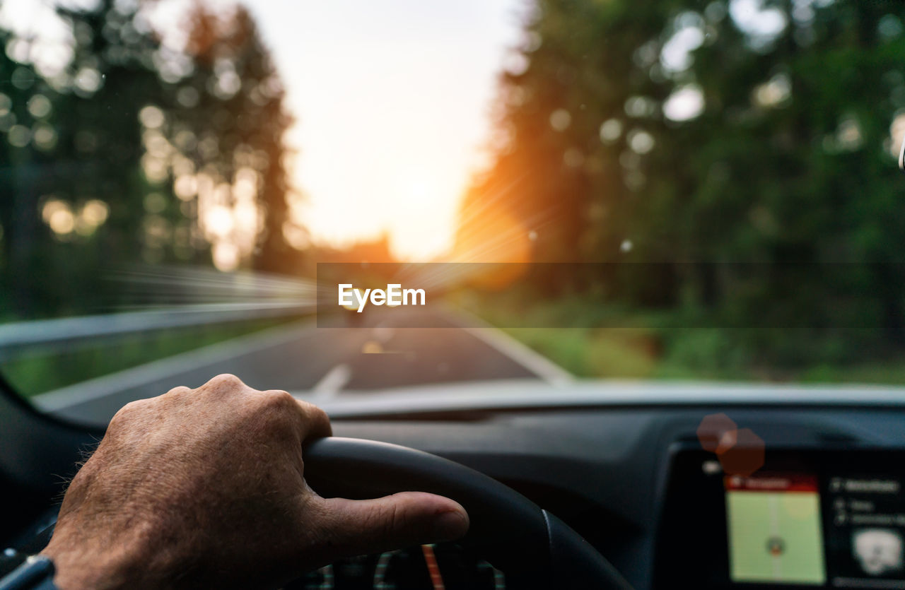 Cropped hand of man driving car during sunset