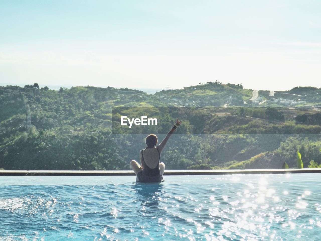 Rear view of woman showing peace sign at poolside against mountain