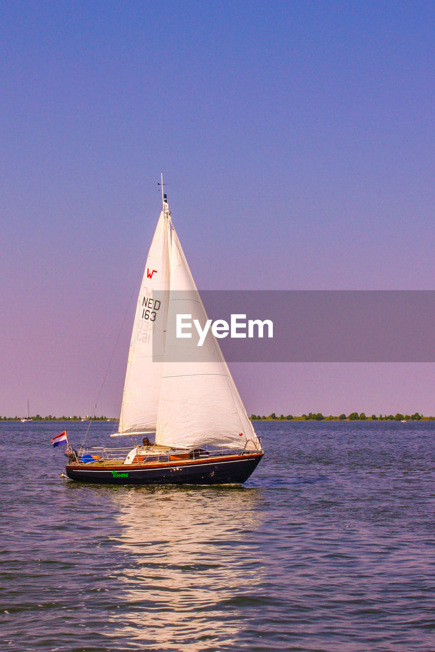 SAILBOAT SAILING IN SEA AGAINST CLEAR BLUE SKY