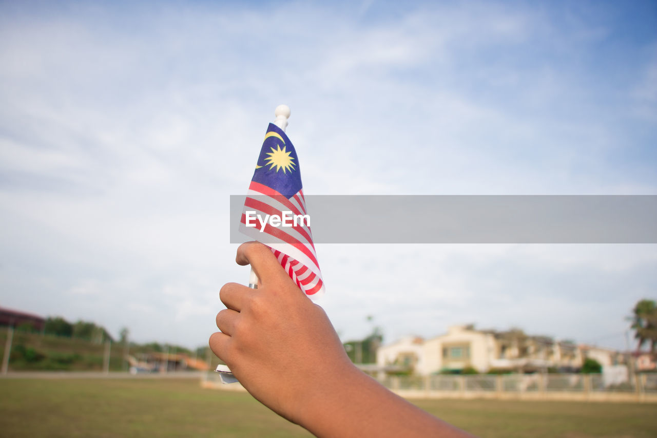 Cropped image of person holding malaysian flag against sky