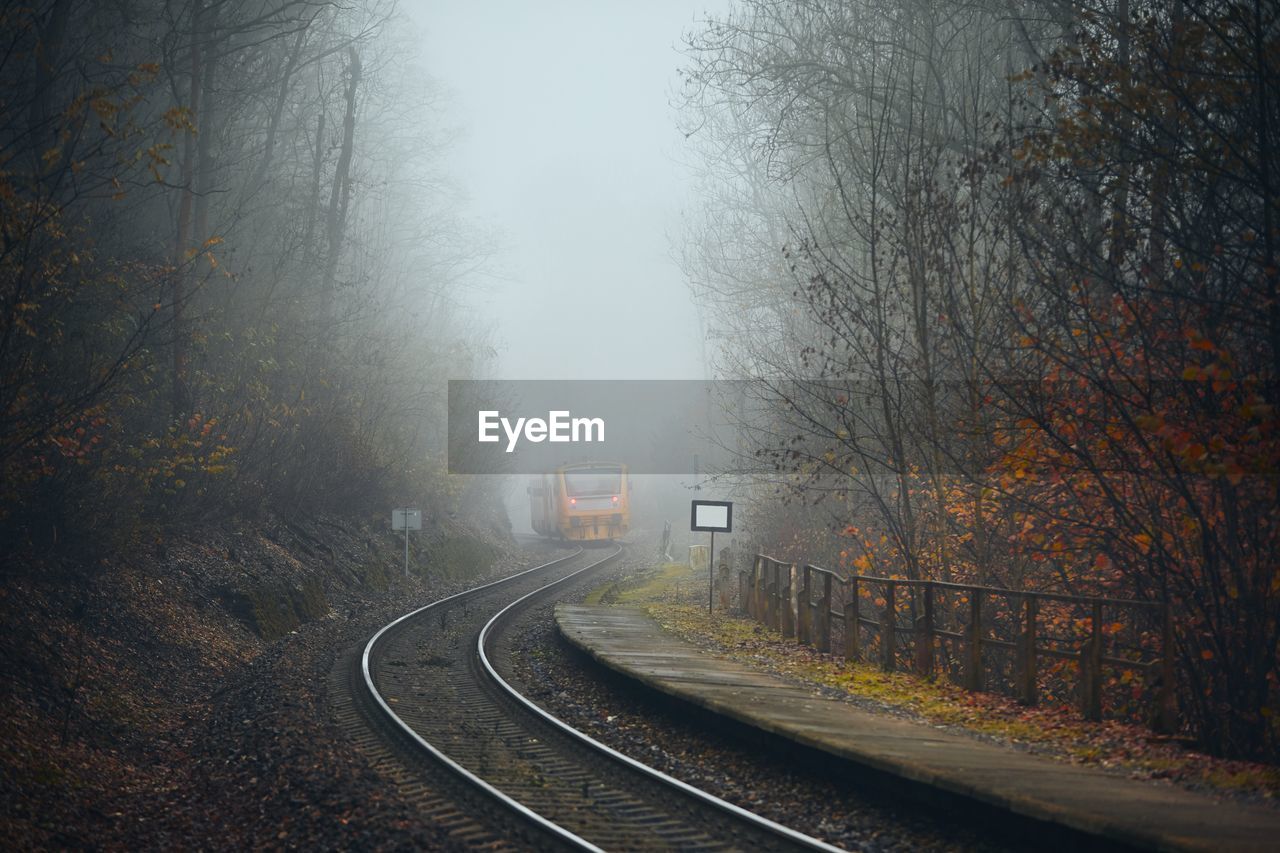 Railway during autumn weather. passenger train leaving railroad station in foggy forest.