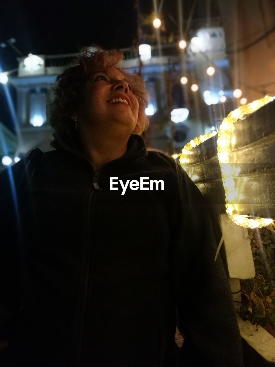 Smiling mature woman looking at illuminated lights at night