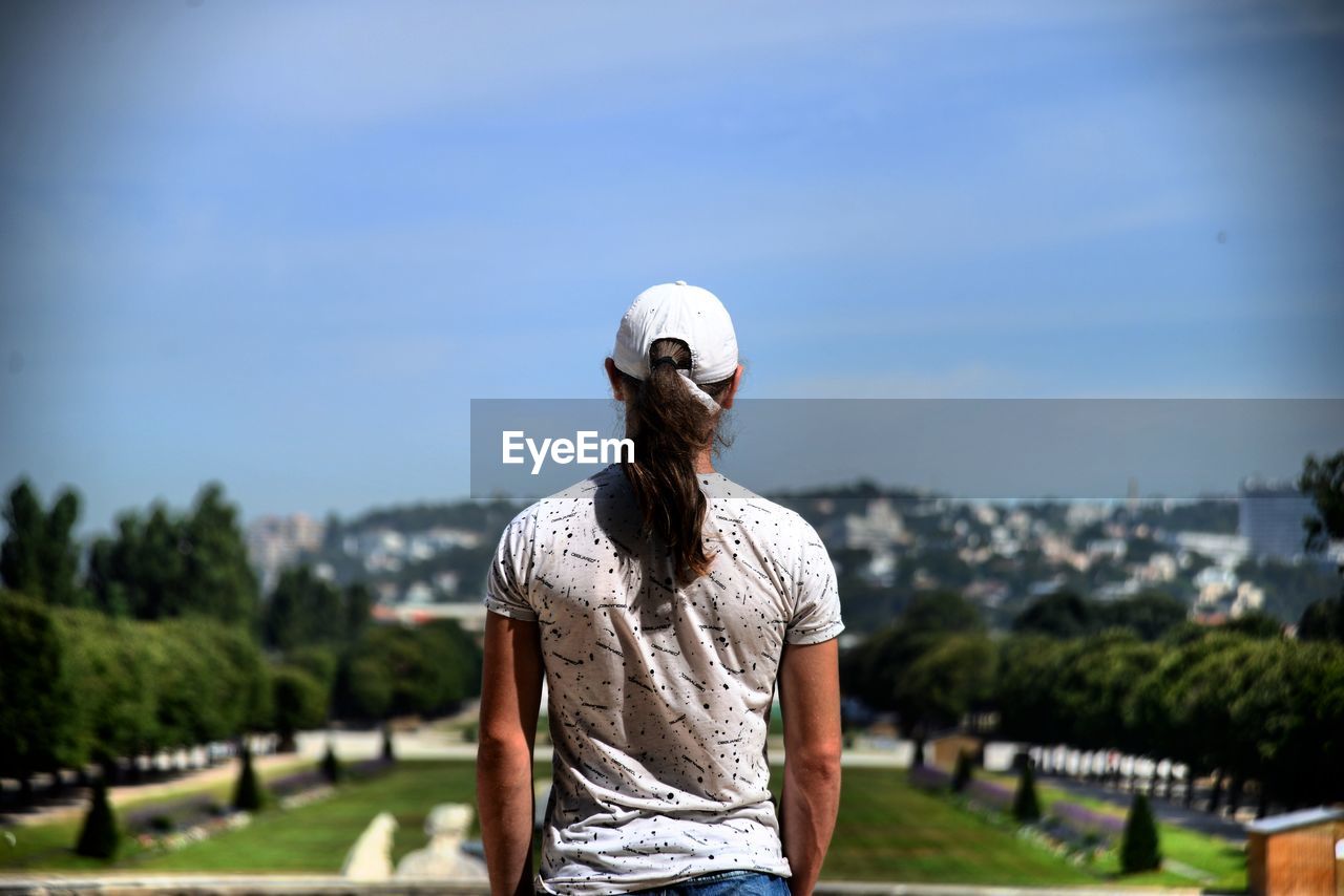 REAR VIEW OF WOMAN STANDING AGAINST WALL