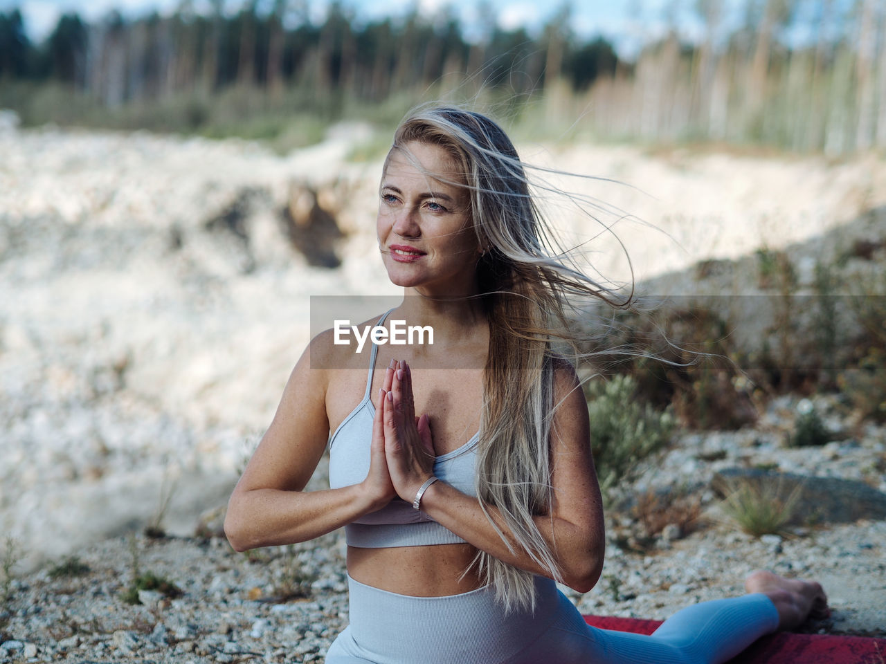 Young beautiful blond woman with long hair in activewear doing leg-split in outdoor training in hill