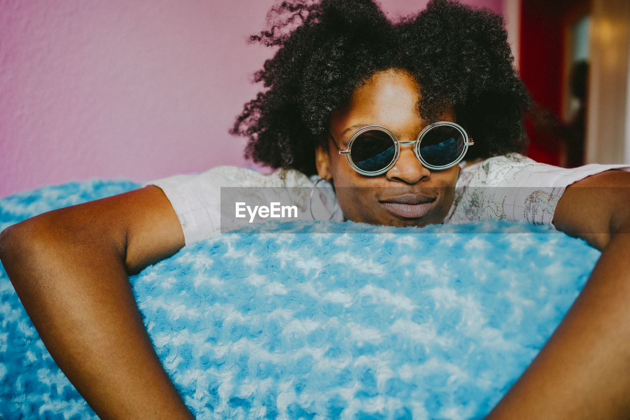 Young hipster woman with sunglasses lying on blue blanket at home