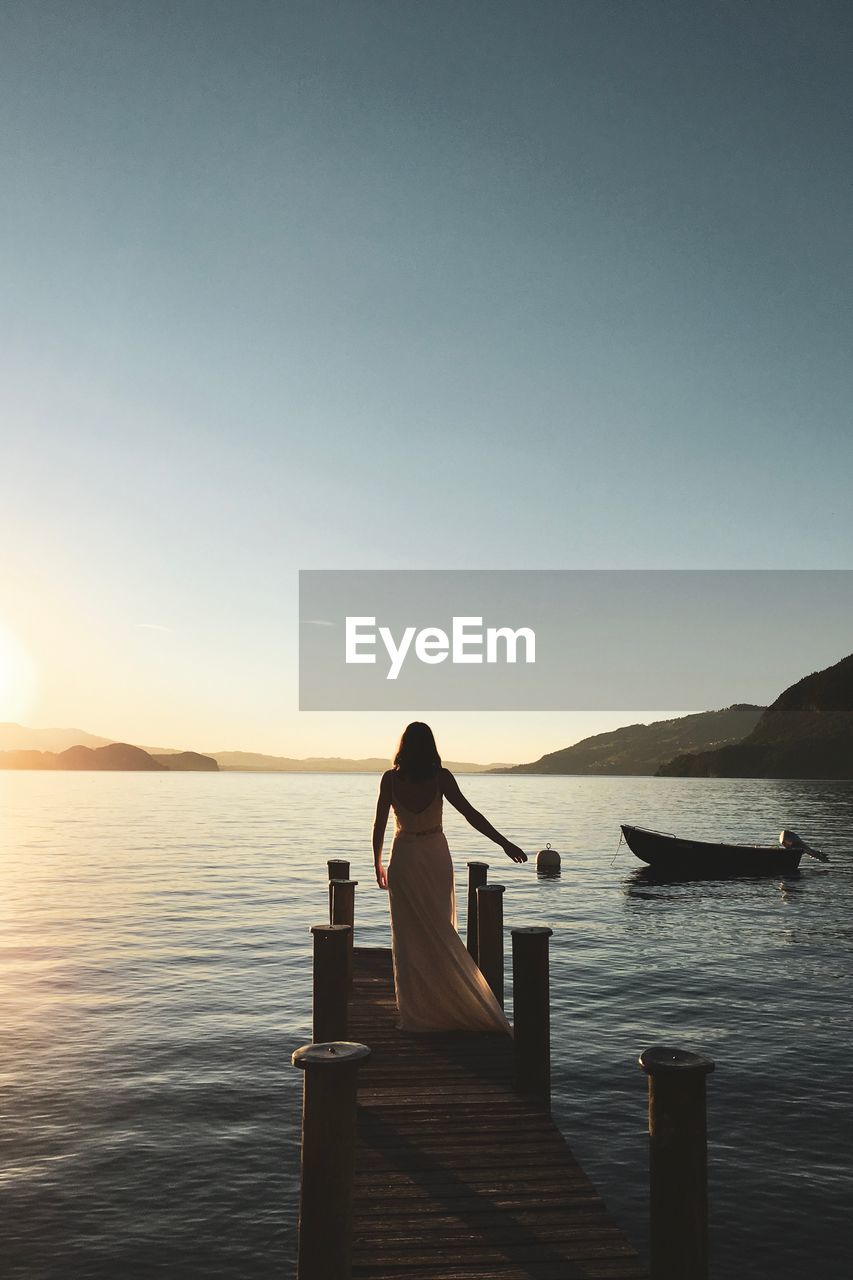 Rear view of woman standing on pier by sea against clear sky