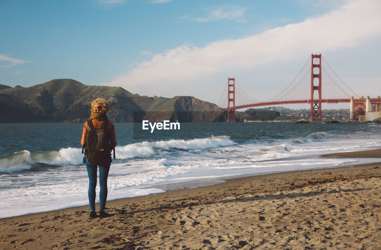 Woman standing on shore with golden gate bridge in background