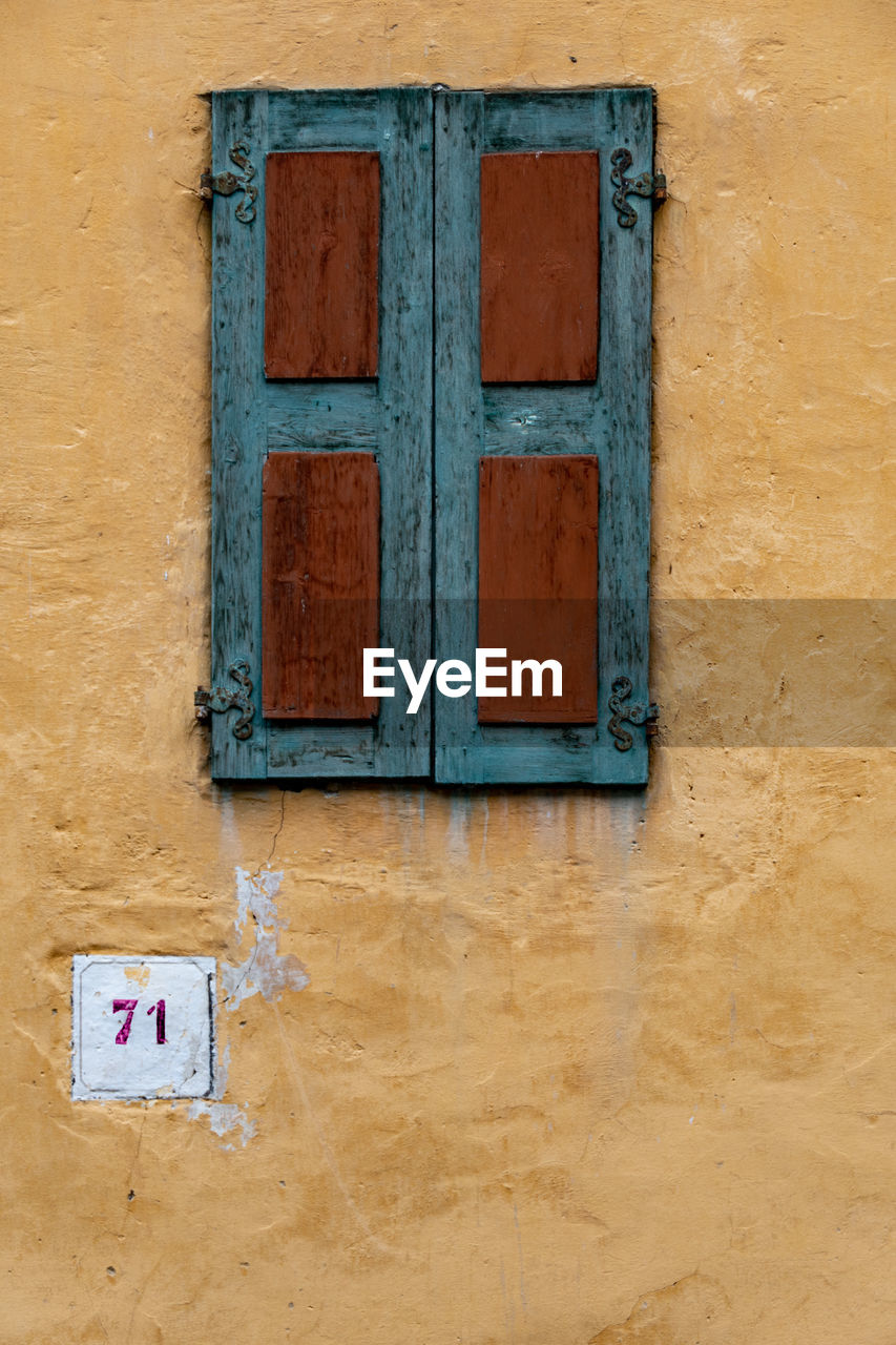 Wooden window in brown and indigo colors on ocher wall at number 71