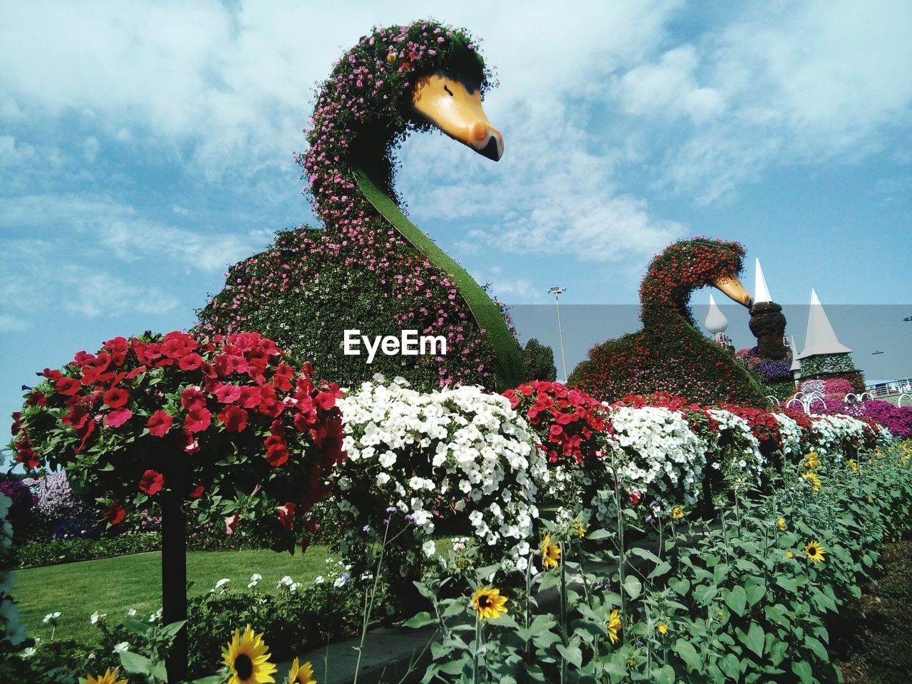 Low angle view of statues and flowers growing against sky in park