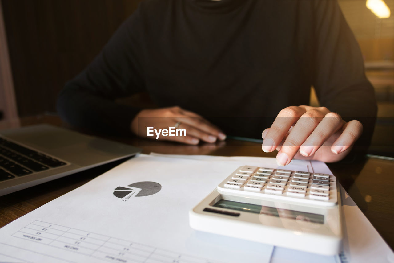 Midsection of person calculating data on calculator at office desk