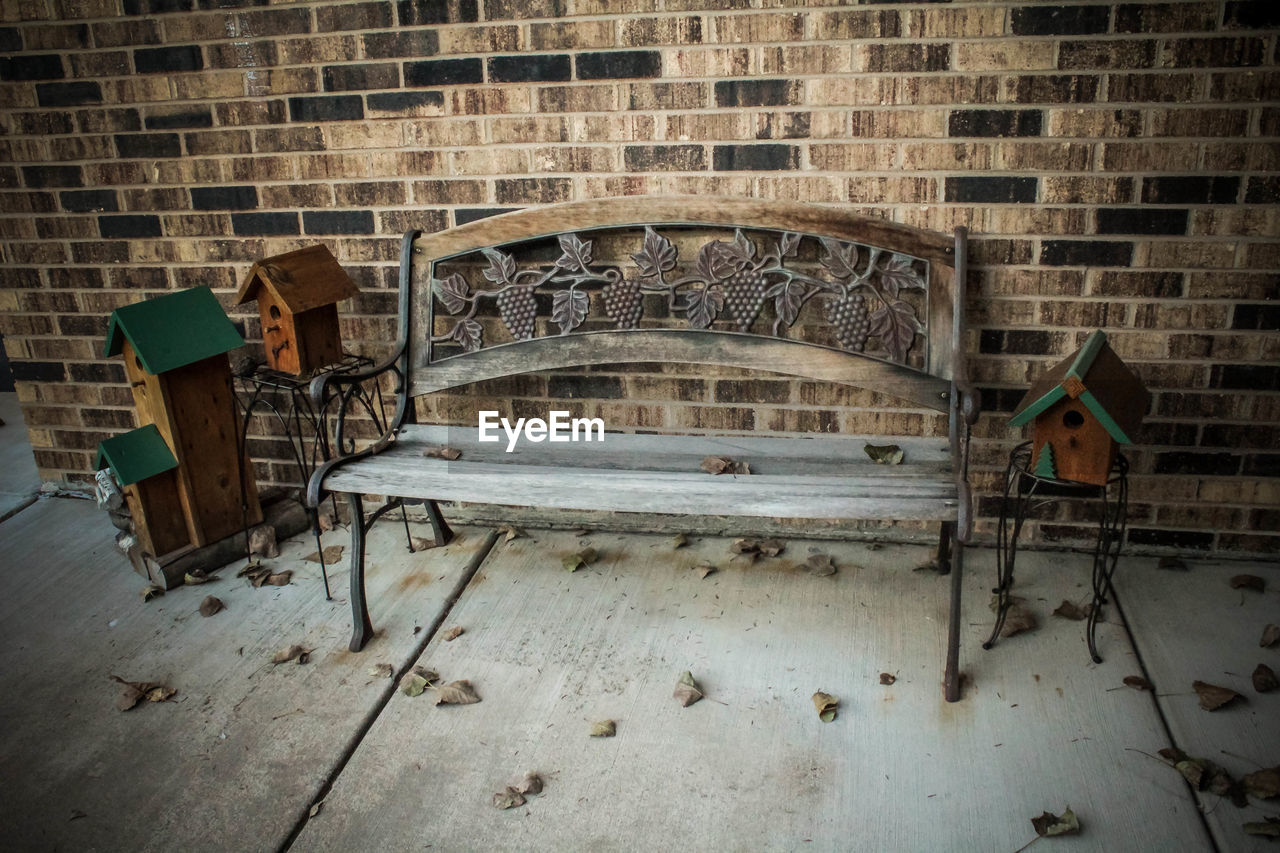 Empty bench on walkway against brick wall