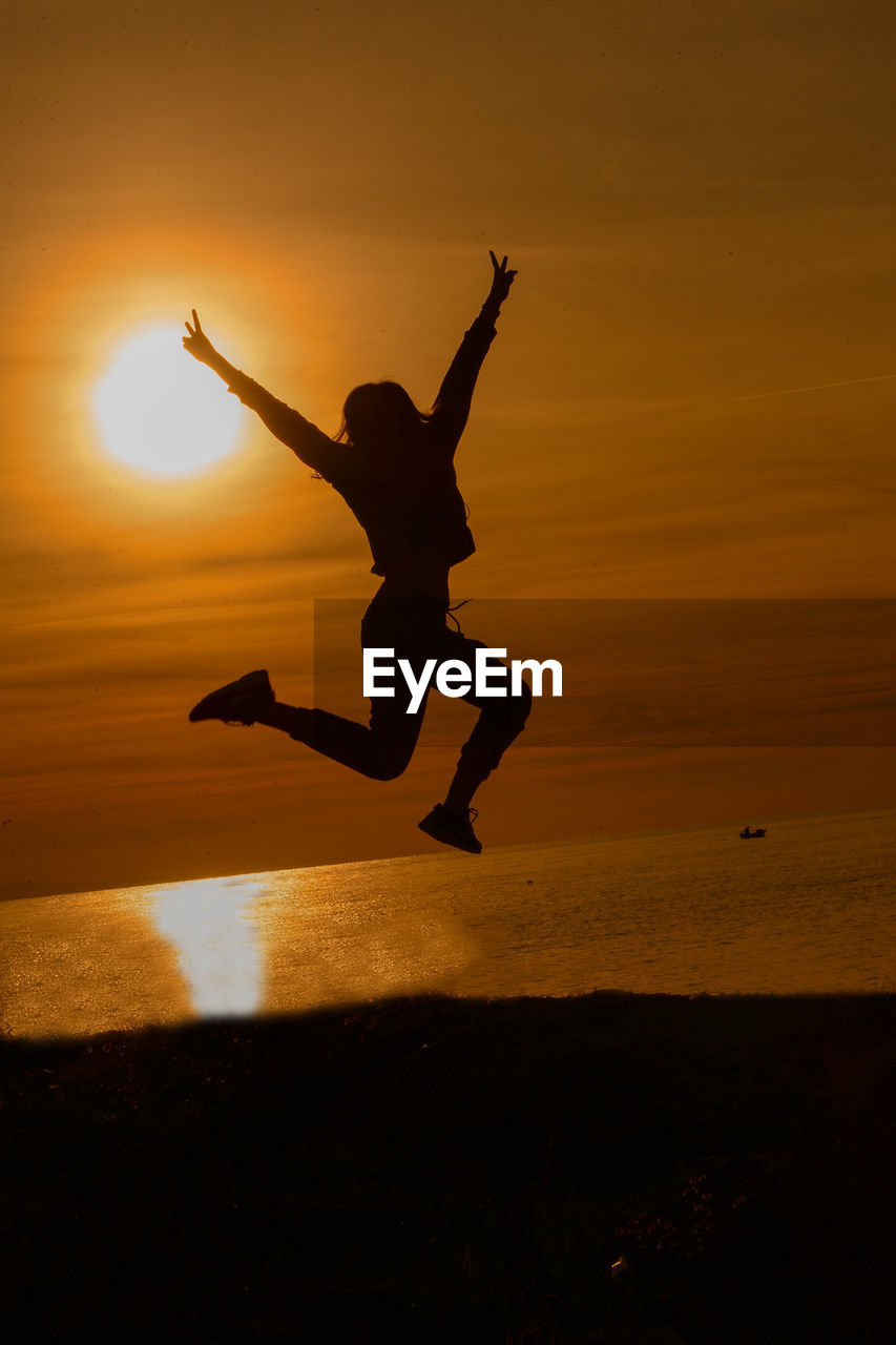 Silhouette man jumping on beach during sunset