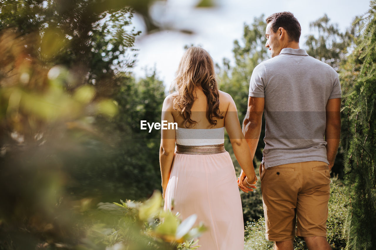 Rear view of couple holding hands while walking at park