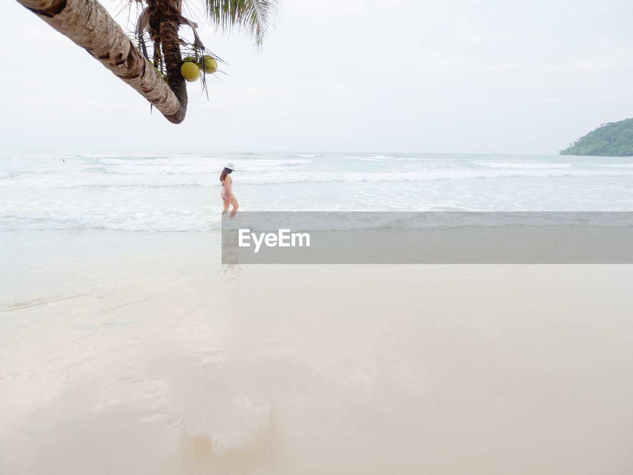 Hipster young woman in bikini walking barefoot on the beach and look to the little waves. 