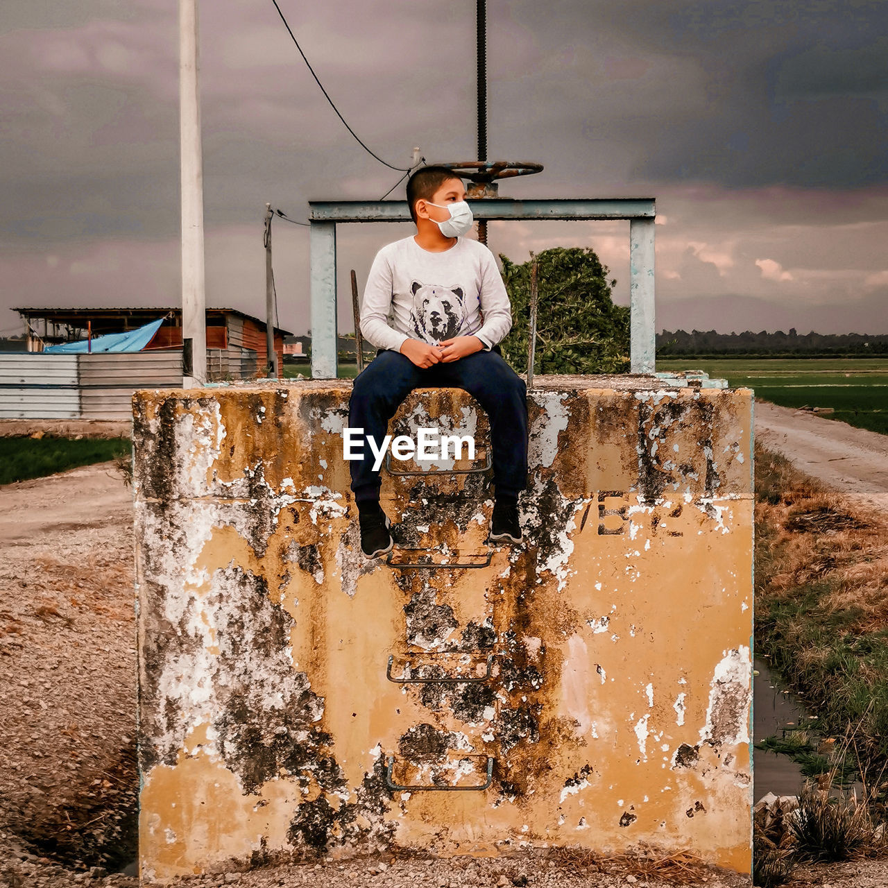 Full length of teenage boy sitting on brick against sky