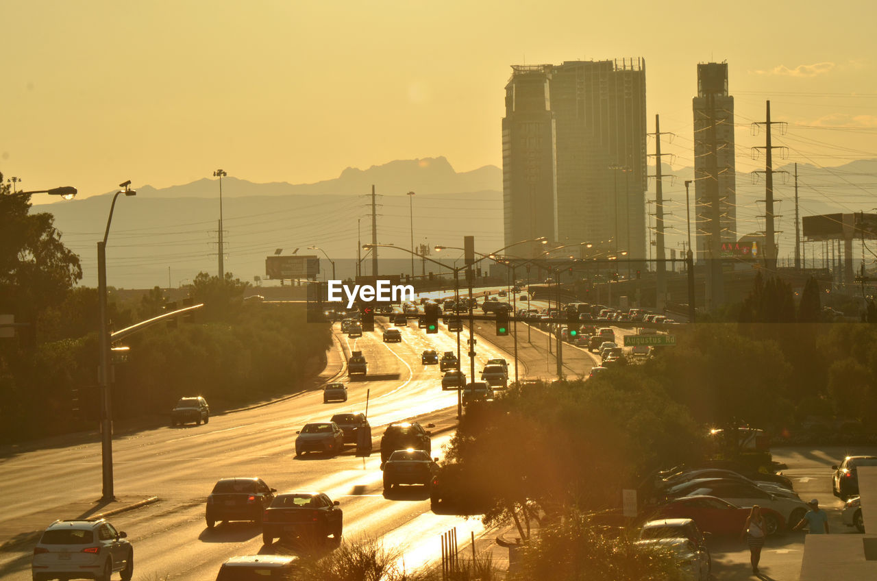 Traffic on road in city against sky during sunset