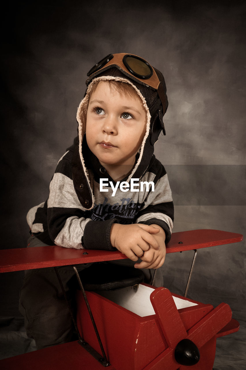 Boy wearing flying goggles with red airplane against gray background