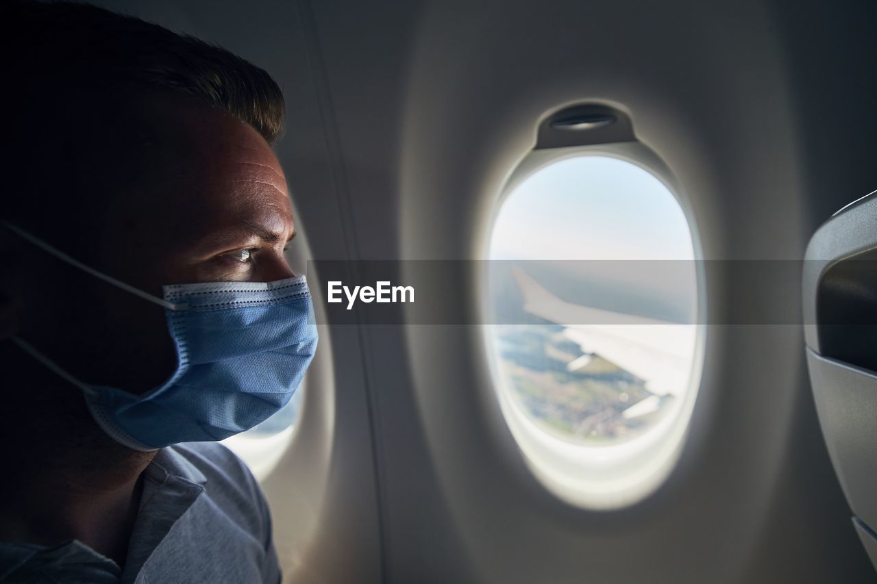 Close-up of man wearing flu mask sitting at airplane 