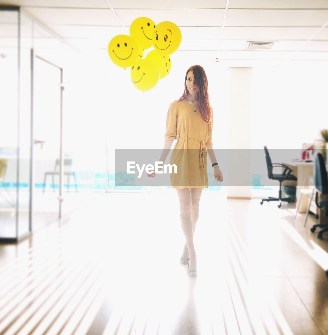 Full length of young woman standing by balloons in office