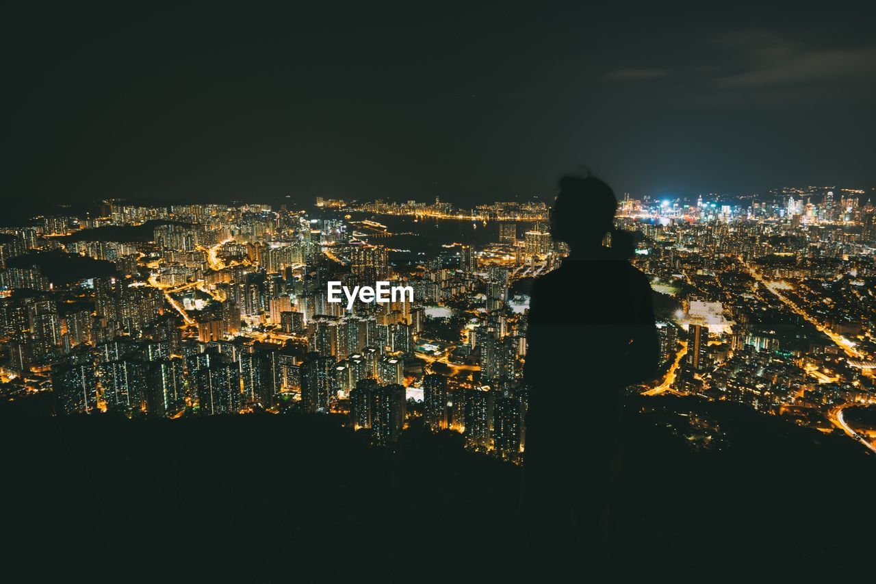 Silhouette person standing against illuminated cityscape at night