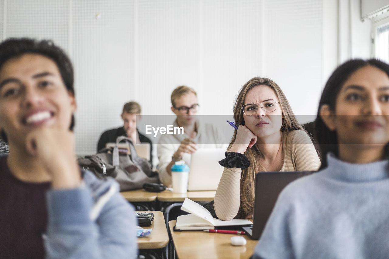 Young woman with friends listening while sitting in classroom