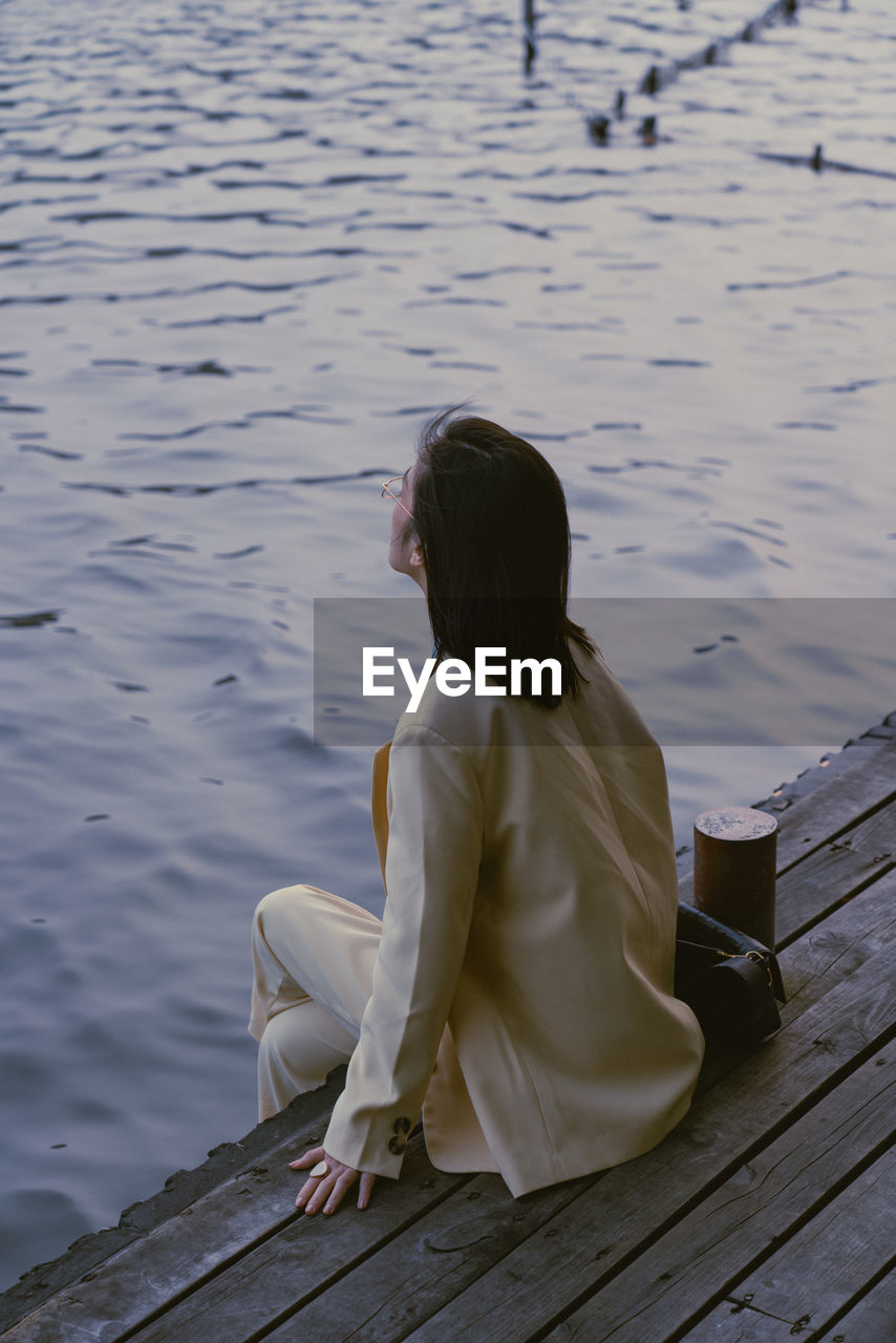 REAR VIEW OF WOMAN SITTING ON PIER