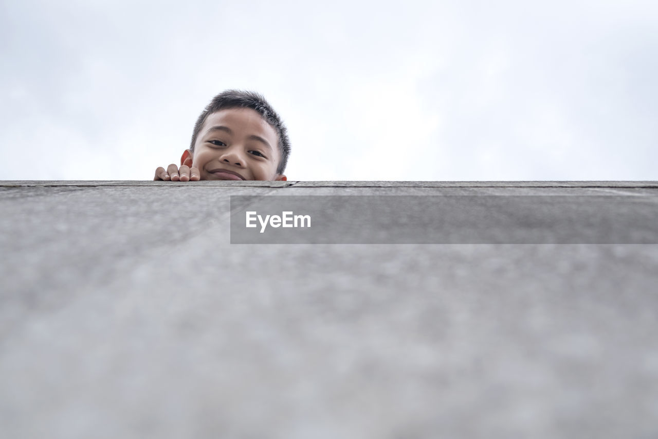 Low angle portrait of boy standing by wall against clear sky