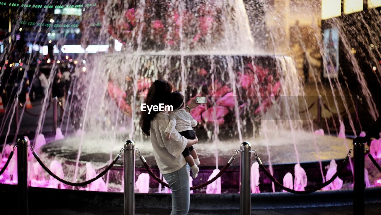 Side view of woman carrying daughter by fountain