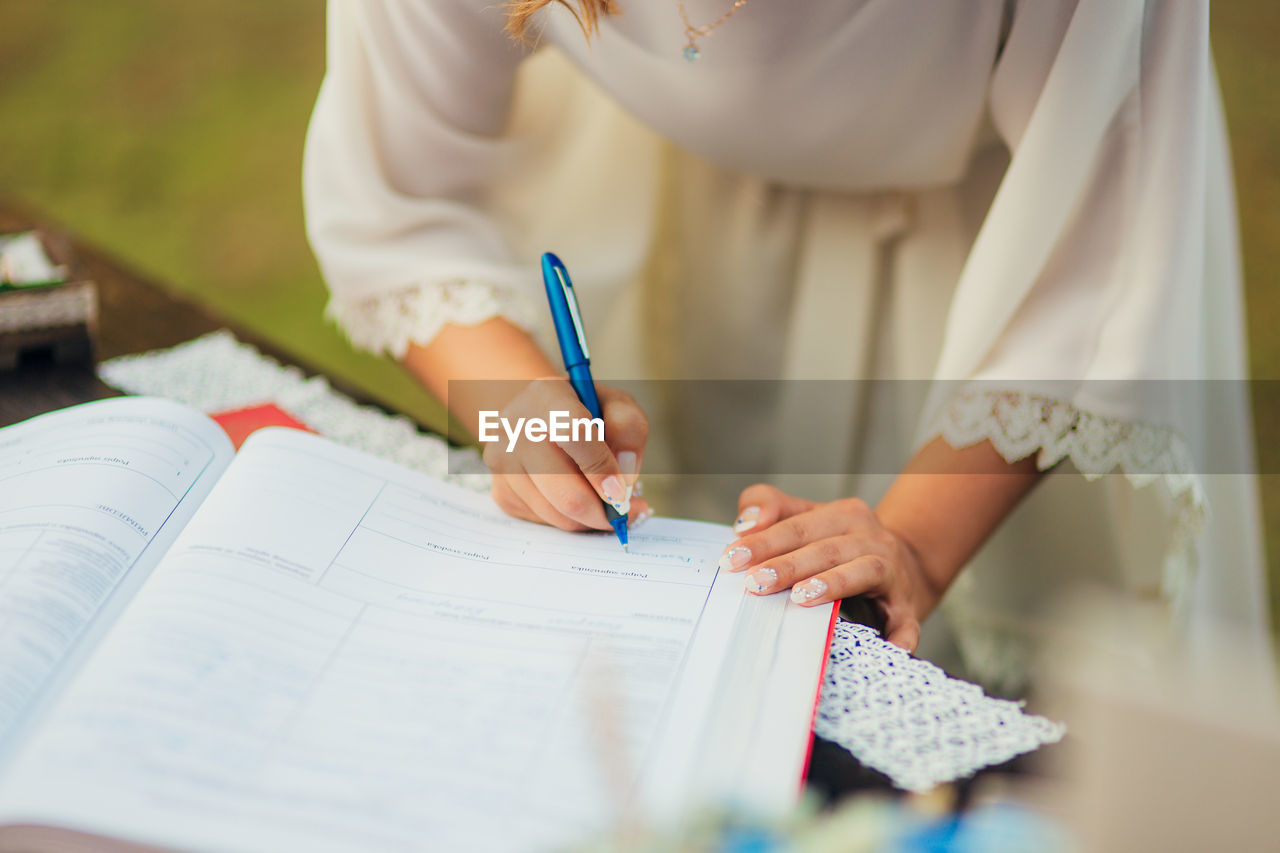 Midsection of woman writing in book on table