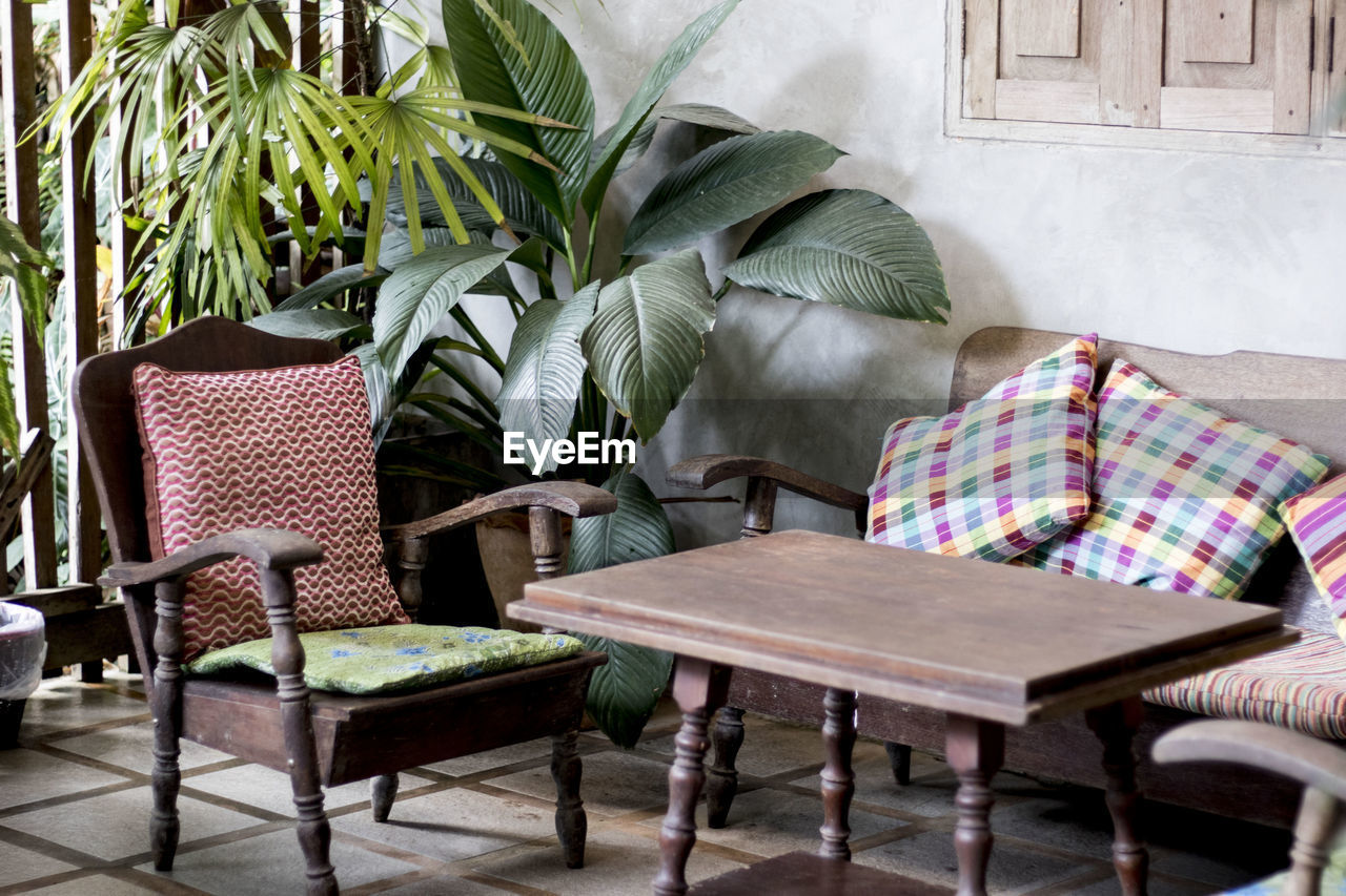 EMPTY CHAIRS AND TABLE BY POTTED PLANTS ON BUILDING