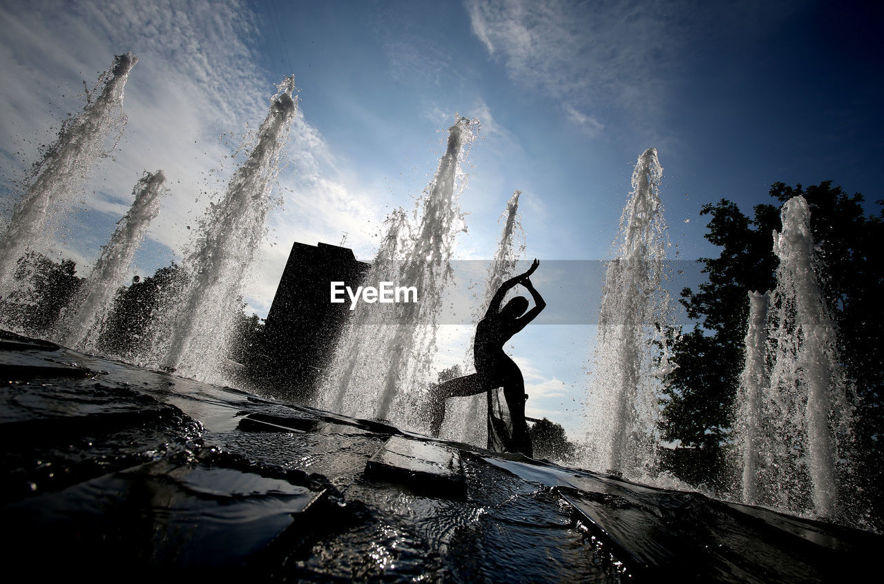 Silhouette woman dancing by splashing water in fountain
