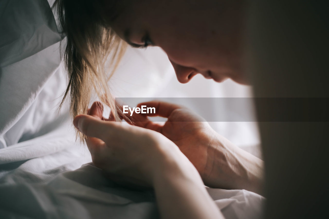 Close-up of woman looking at cupped hands on bed