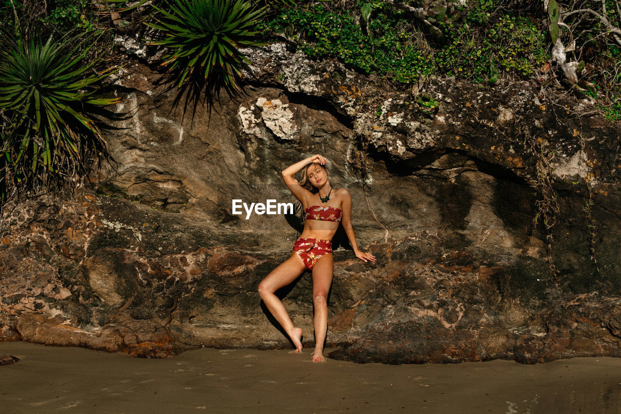 Beautiful young woman wearing bikini against rock formation at beach