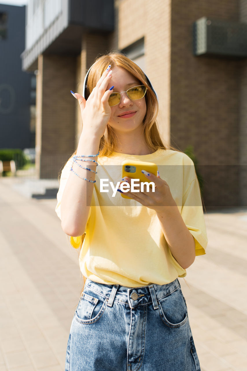 Happy teenager girl in a yellow shirt is holding a cell phone