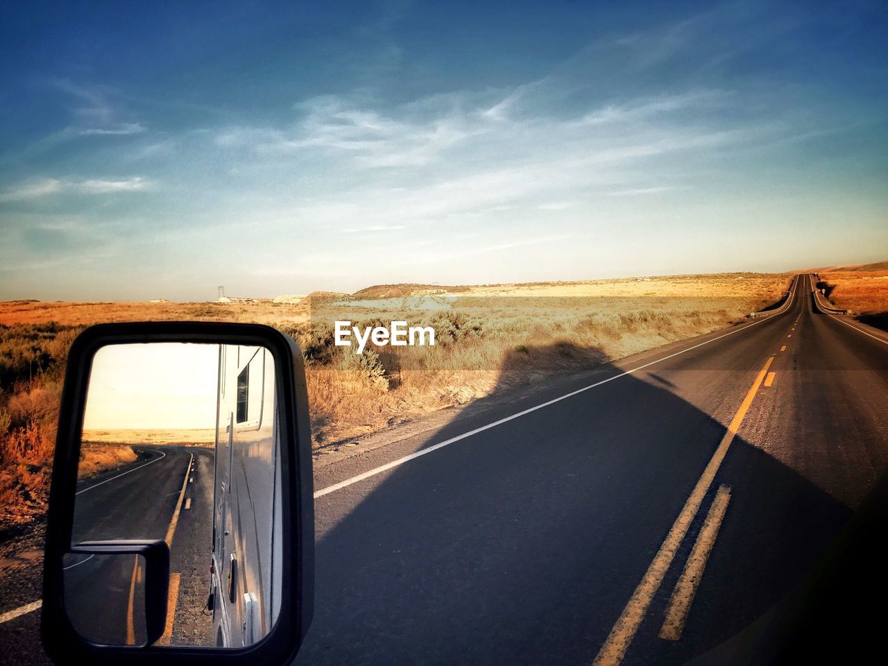 Vehicle reflecting in side-view mirror on road against sky