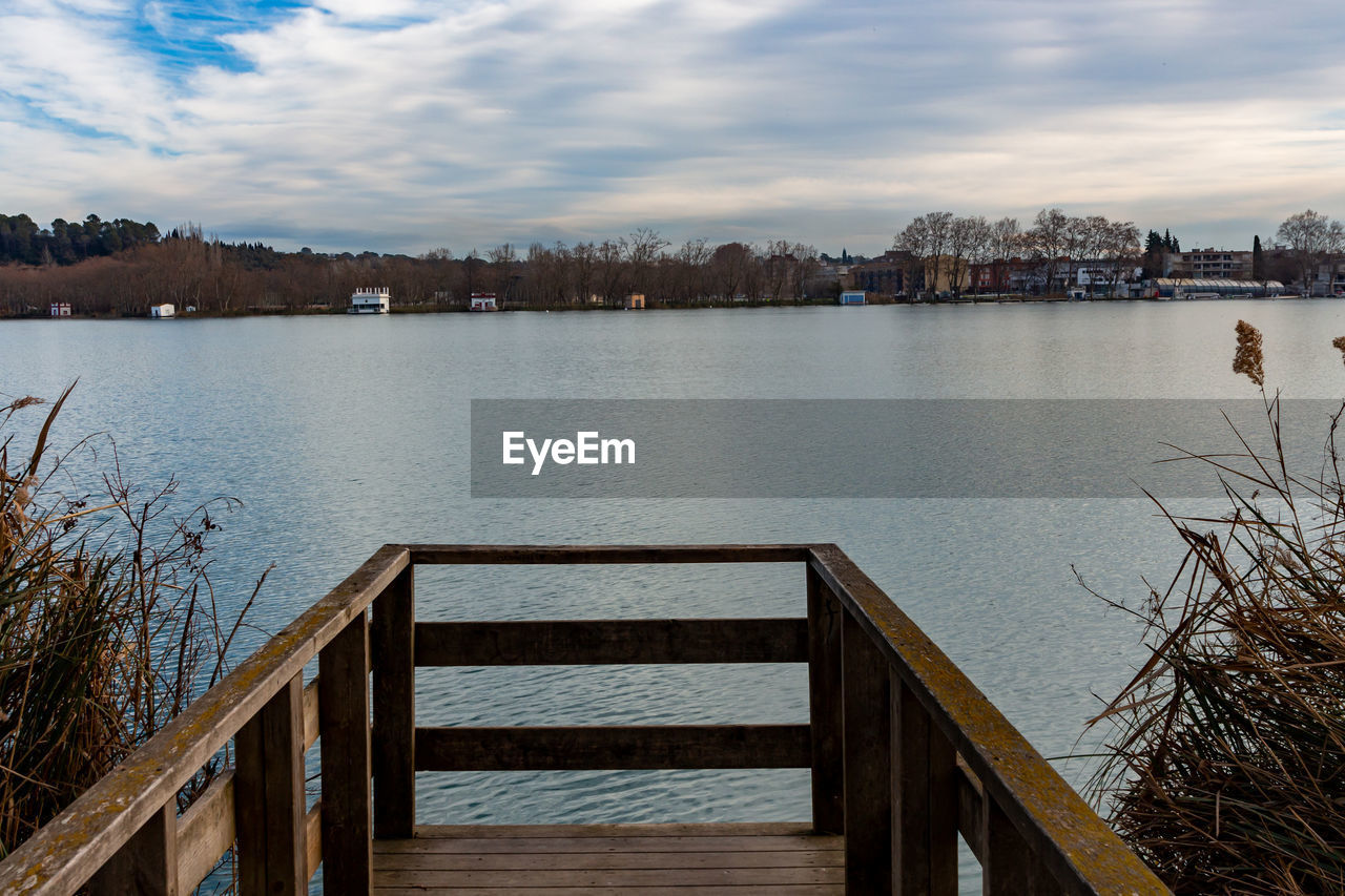 water, reflection, architecture, sky, morning, built structure, cloud, nature, river, scenics - nature, city, shore, travel destinations, tranquility, building exterior, beauty in nature, no people, body of water, landscape, pier, wood, tranquil scene, tree, railing, dock, reservoir, outdoors, building, winter, bridge, environment, tourism, travel, dusk, plant, day, beach, land