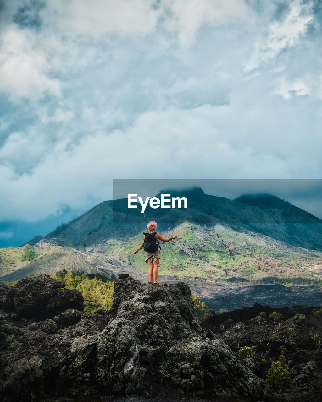 Hiker standing on rock looking at mountain against sky