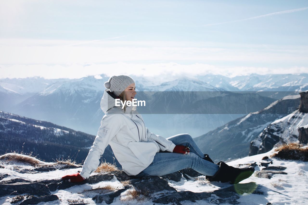 Side view of woman sitting on snowy mountain peak