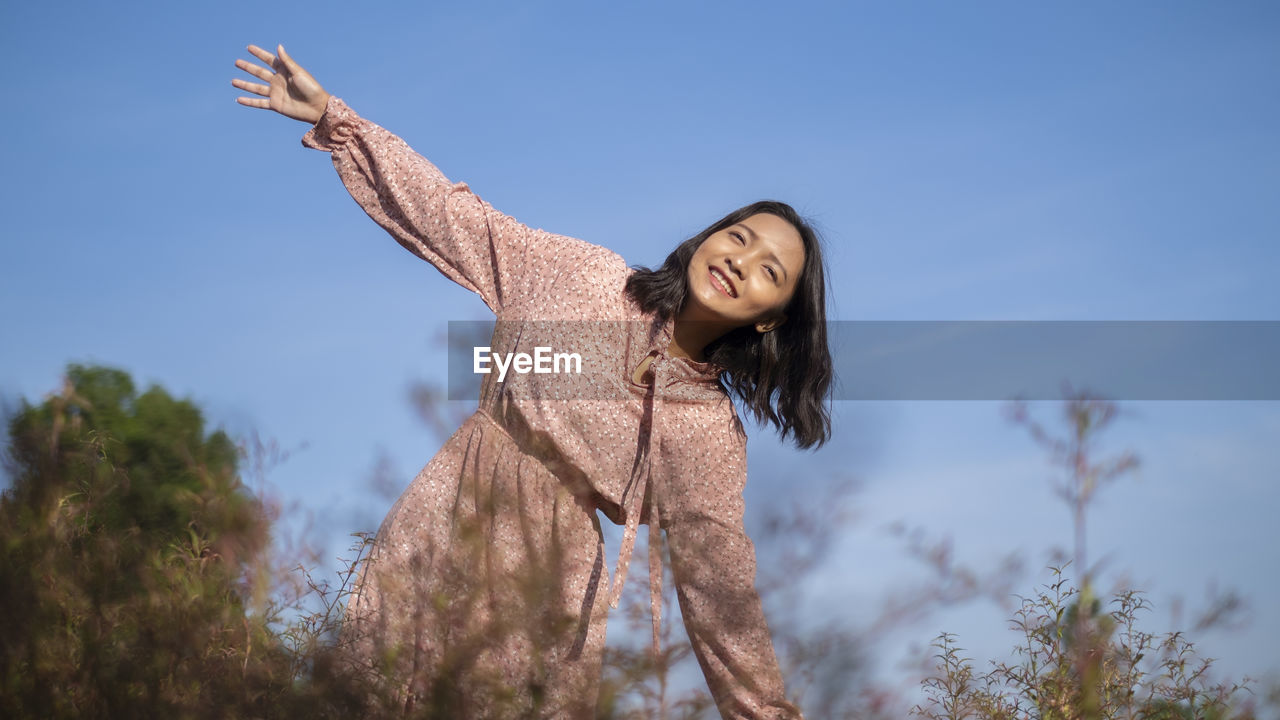 YOUNG WOMAN WITH ARMS OUTSTRETCHED AGAINST SKY