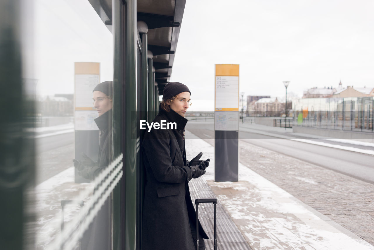 Young man waiting at bus stop in winter