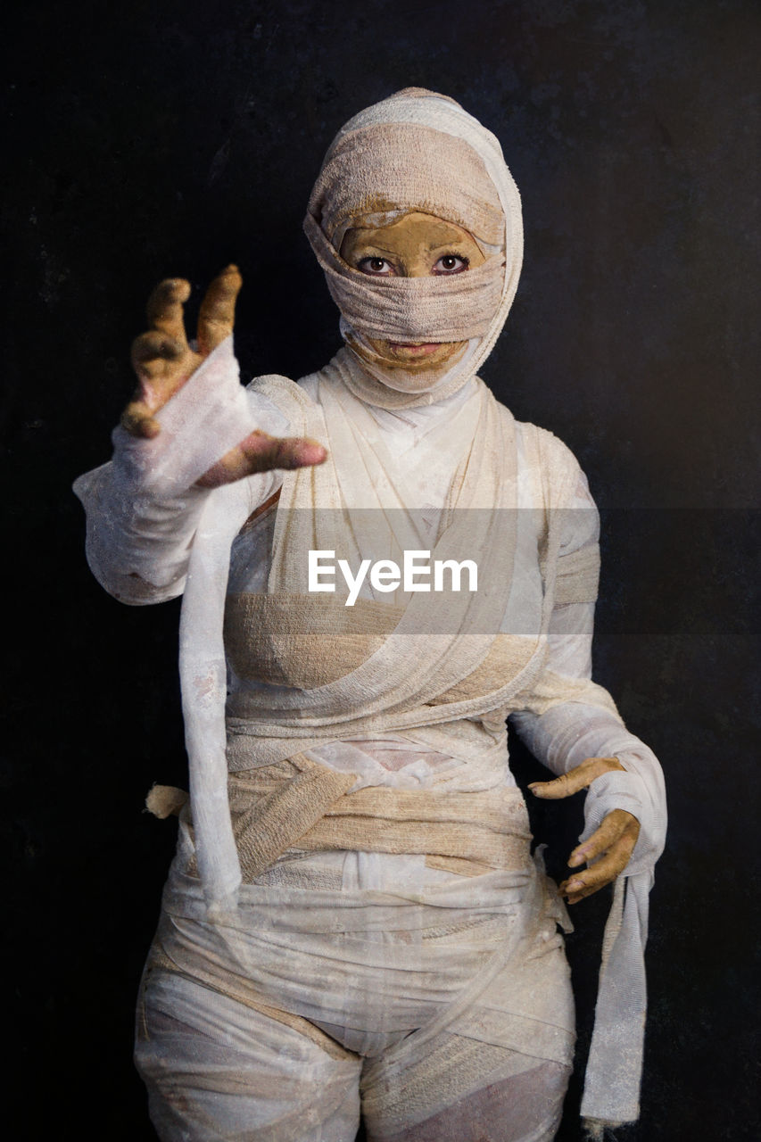 Portrait of woman in mummy costume during halloween standing against black background