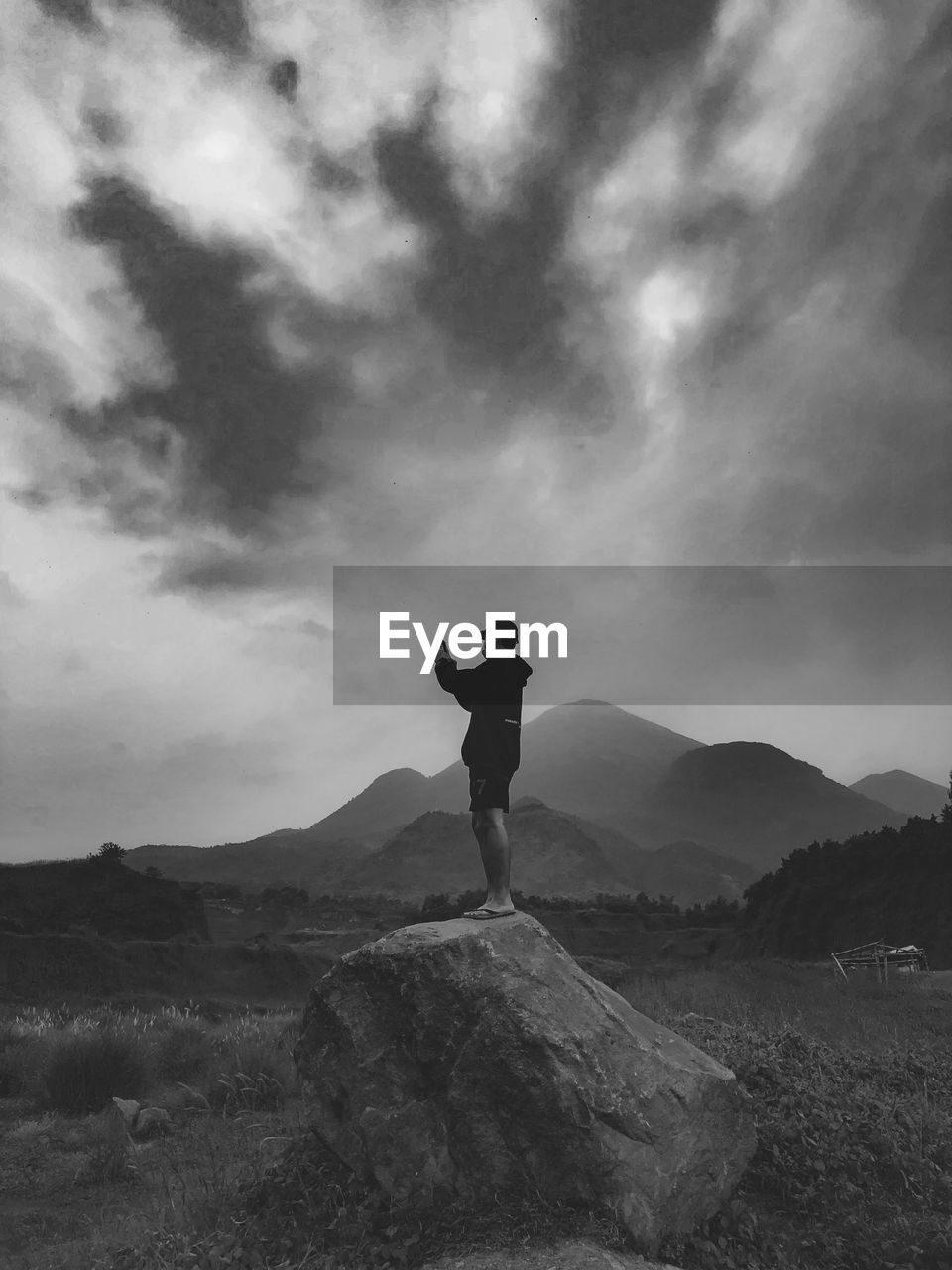 MAN STANDING ON ROCK AGAINST MOUNTAIN