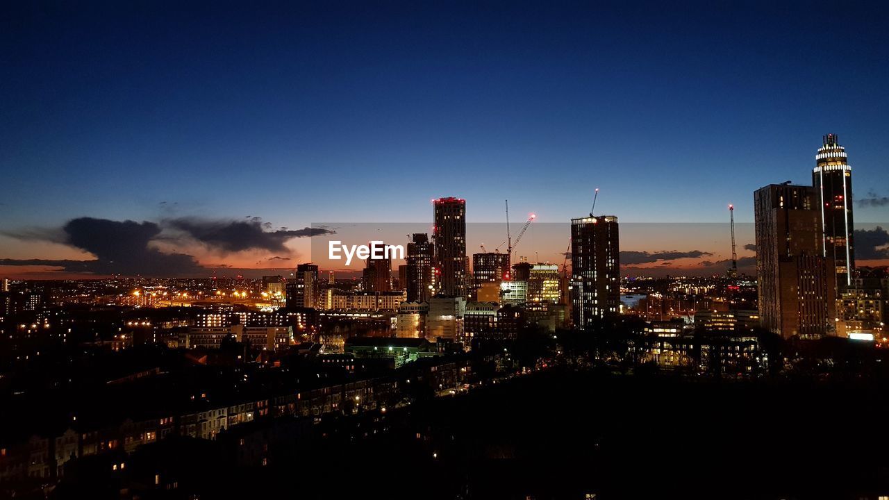 VIEW OF ILLUMINATED CITYSCAPE AGAINST BLUE SKY