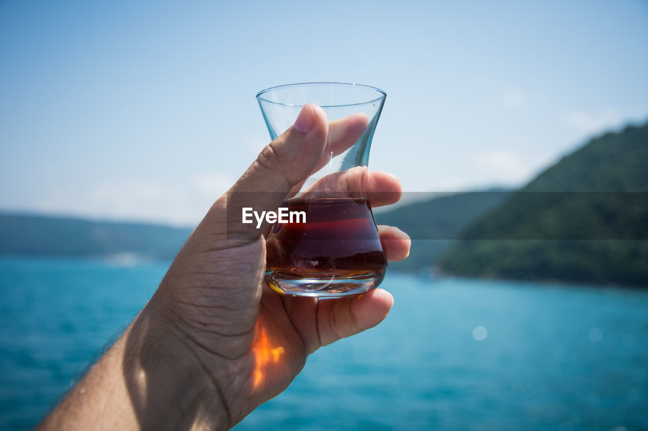 Close-up of hand holding alcohol against sea