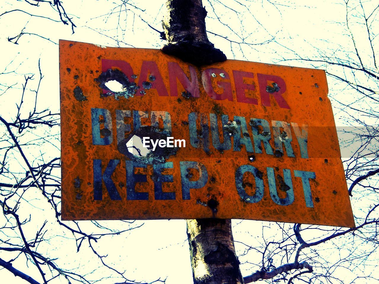 Low angle view of danger sign against sky