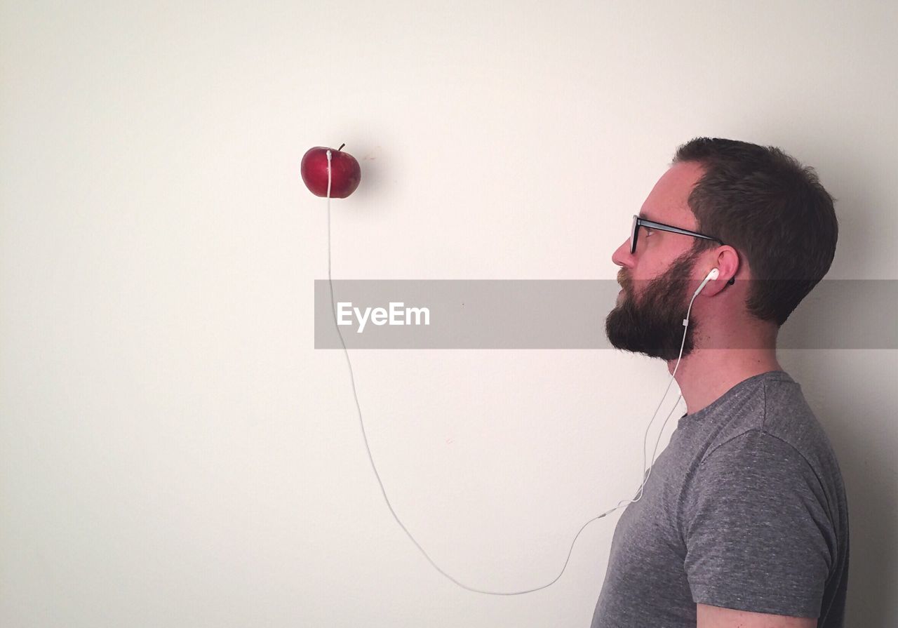 Side view of man with headphones attached to apple on white wall