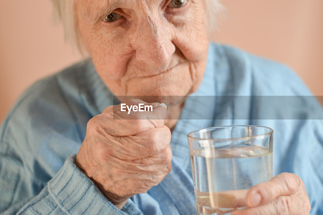  an elderly 90-year-old gray-haired woman who holds a tablet and a glass of water in his hands. 