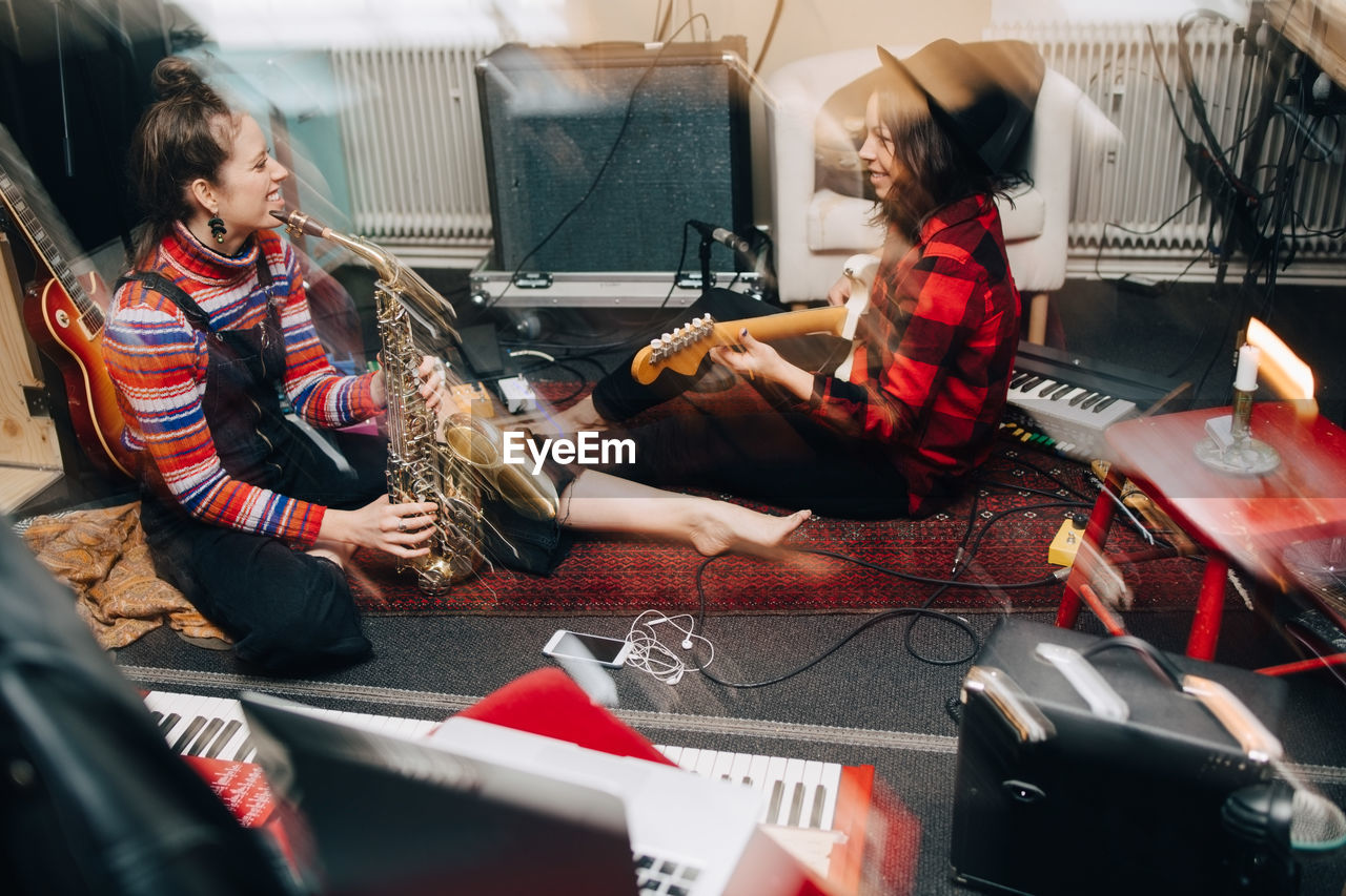 Smiling female musicians playing instruments while sitting on carpet at studio