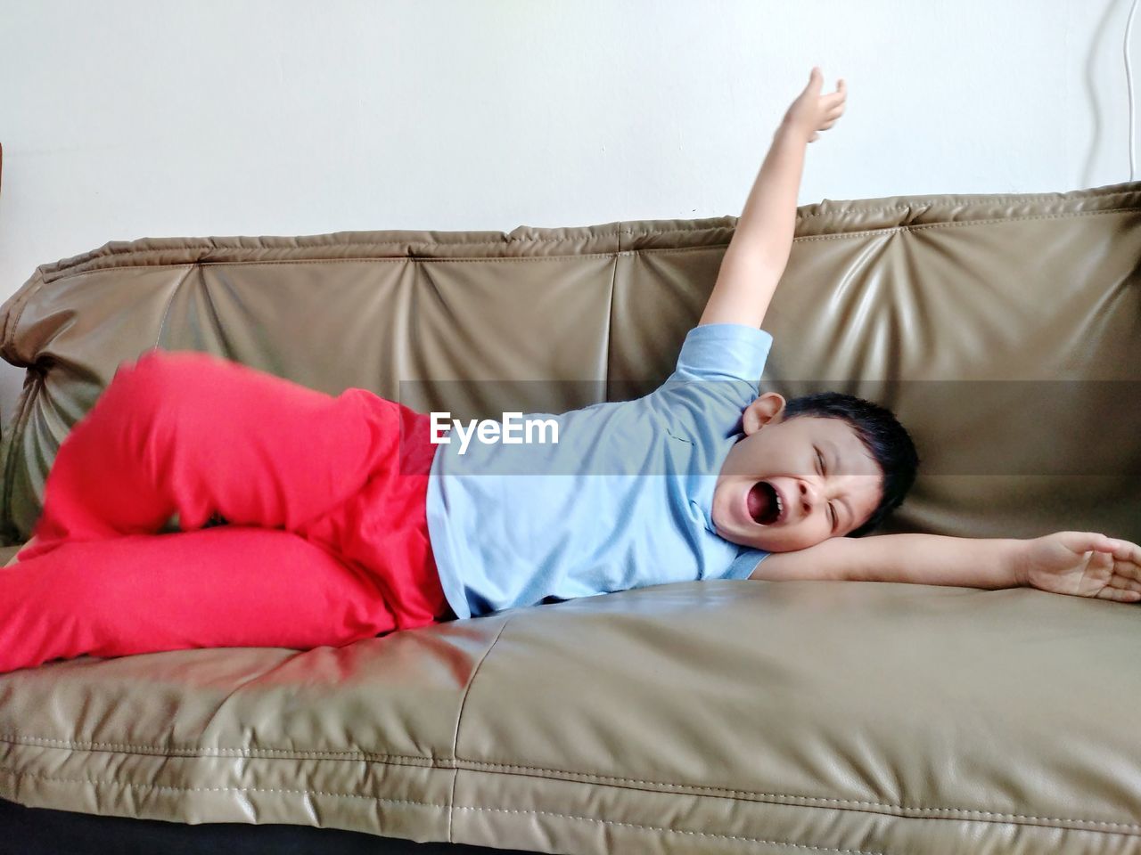 Boy yawning while lying on sofa at home